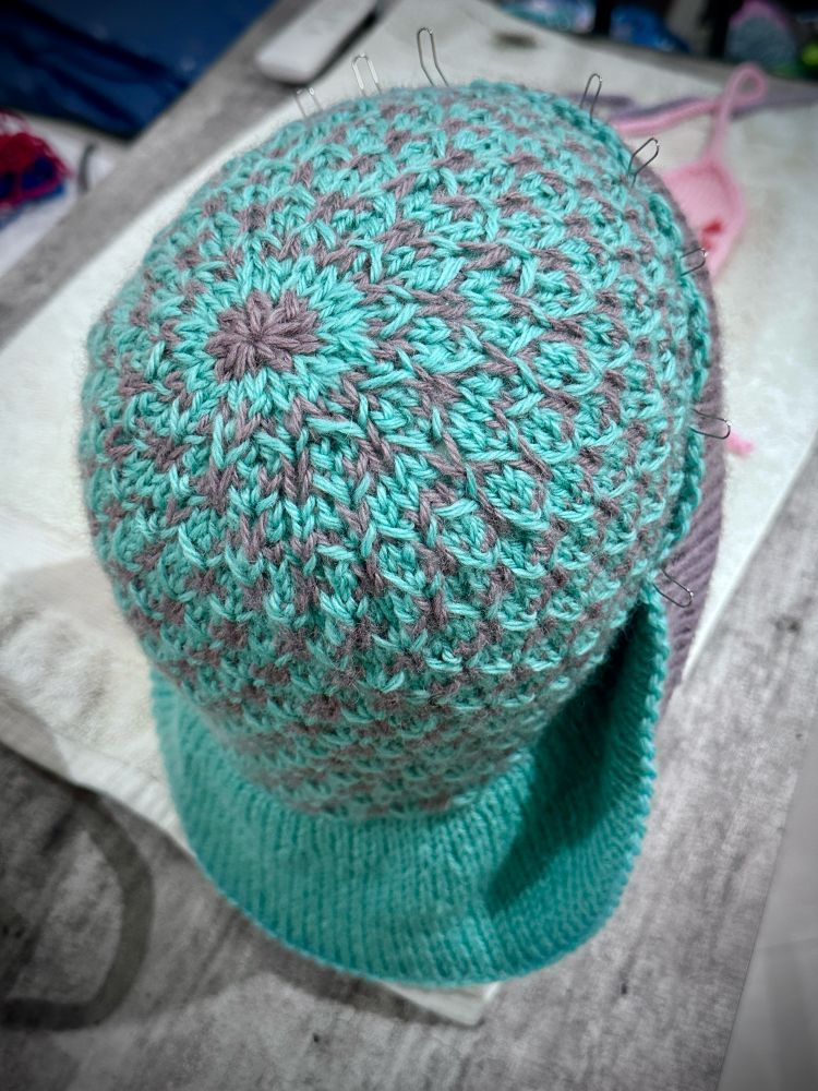 Crown of Hand knit cloche hat shaped on styrofoam mannequin. Cloche hat worked in texture two color slip stitch pattern of green and purple. 