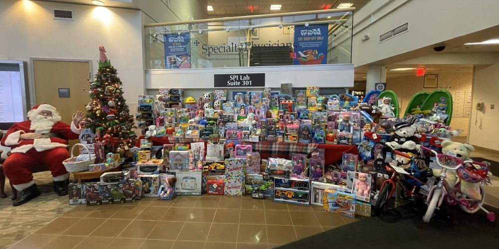 A collection of toys and gifts with Santa Claus seated beside a large decorated Christmas tree.