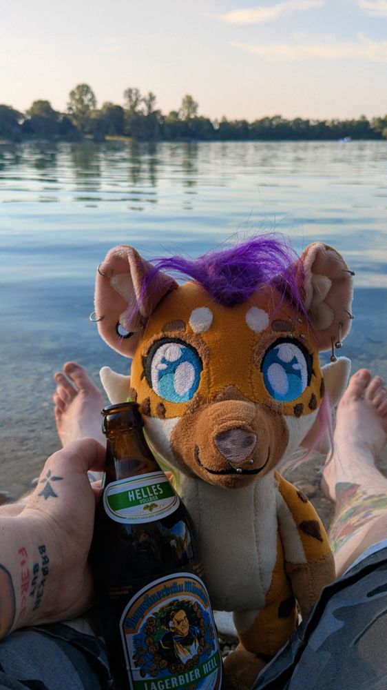 Picture of my Sona plushy with an Helles beer, we see my feet in the water of a lake uwu