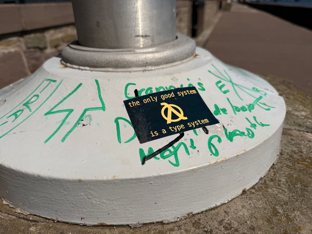 A rectangular black sticker, with yellow writing, saying “the only good system is a type system” with a centred lower case lambda in a circle. 