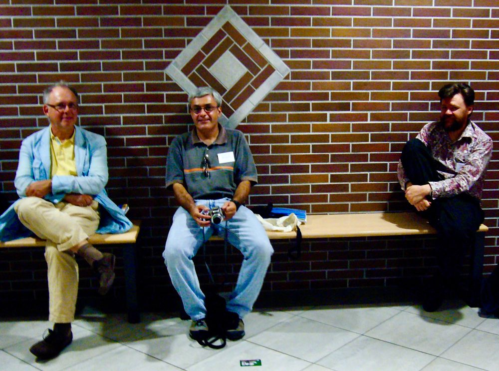 Three men, seated on a bench, in front of a brick wall.

From left to right, Albert Visser, in a blue jacket over yellow shirt and trousers, Aldo Antonelli, in a grey shirt and jeans, holding a camera, and to the right, Greg Restall, in a paisley shirt and dark jeans.