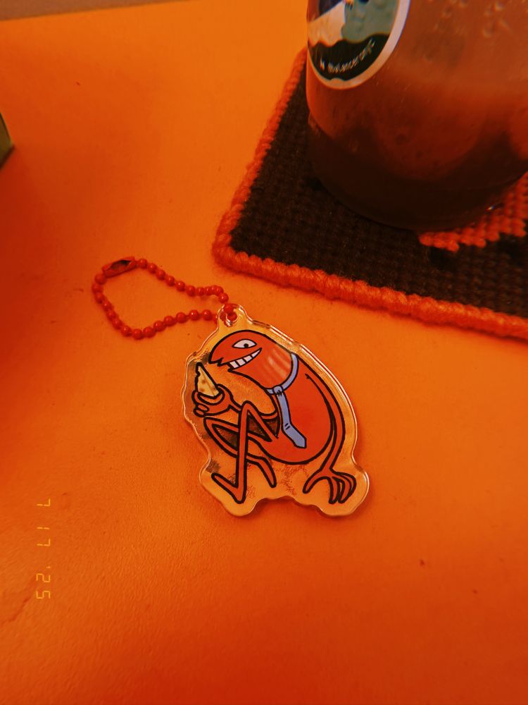 a really cute acrylic charm of allan from smiling friends. he's holding his little piece of swiss cheese and smiling. you might say he is..... a smiling friend. i got this thing in the artist alley at anime nyc last year and i forget who made it but rest assured they were a very cool person