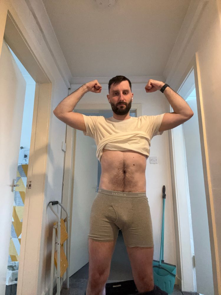 Posing in my hallway both arms up flexing and in underwear with white t-shirt on, showing fitness progress 