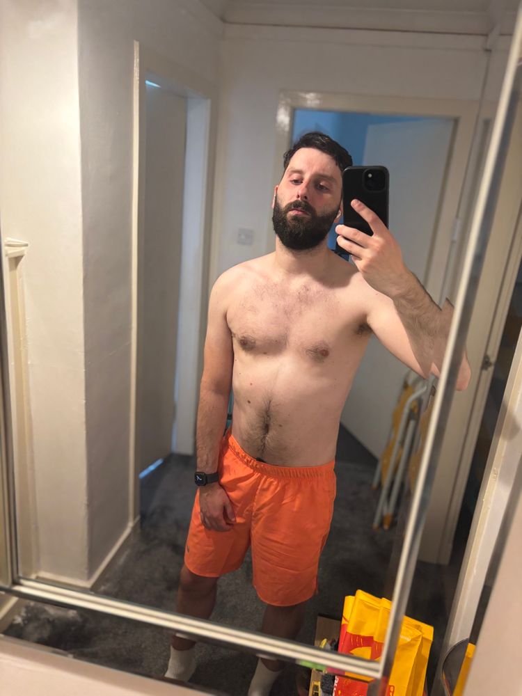 Mirror selfie with bright coral gym shorts and artificial lighting. I don’t have a top on to demonstrate gym progress 