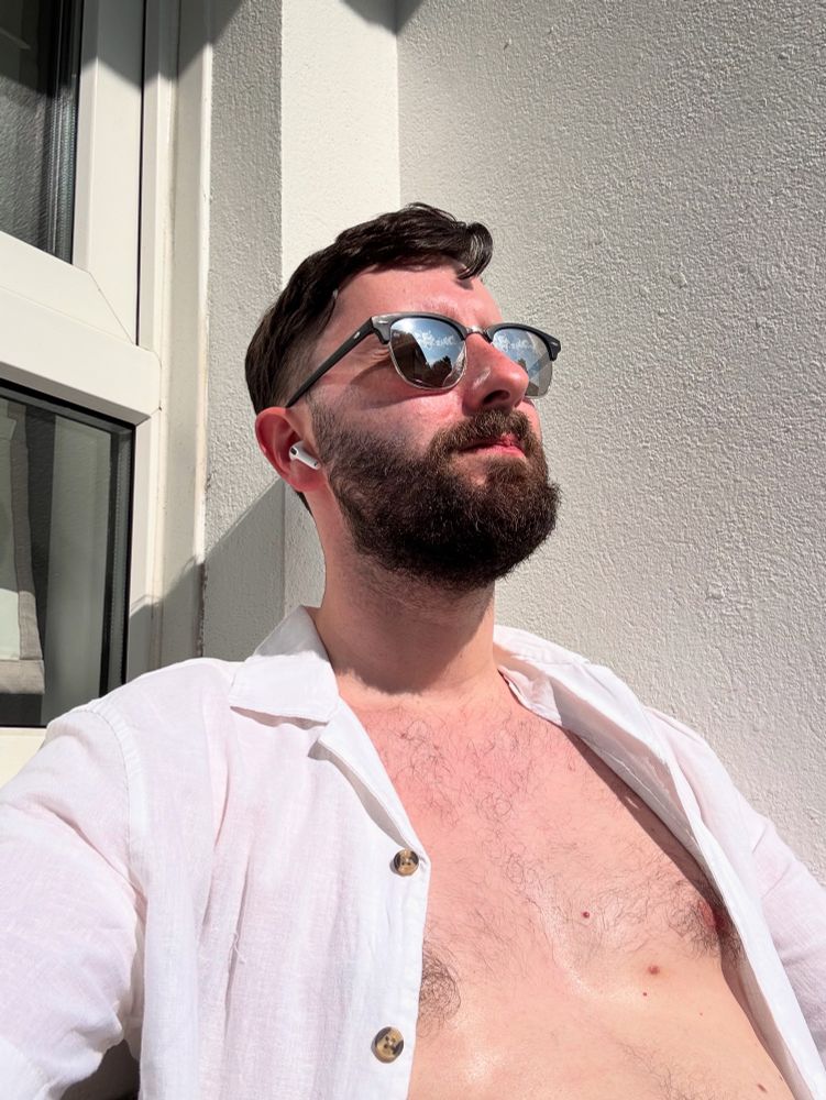 Me on my veranda, sitting sunbathing during a heatwave. I have sunglasses on, white linen shirt and my chest is visible 