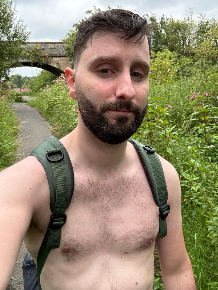 Selfie of myself hiking along a section of cycle route. I am shirtless and have my green backpack on