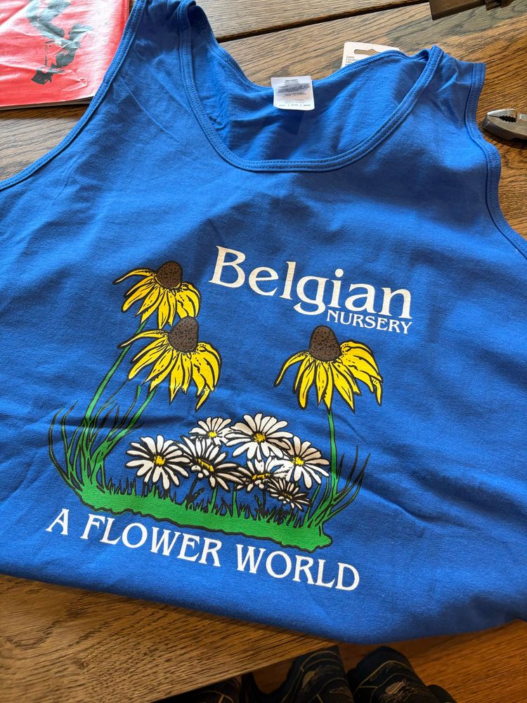 Foto de uma camiseta regata na cor azul royal, com a estampa de flores brancas e amarelas e os dizeres Belgian nursery, a flower world.