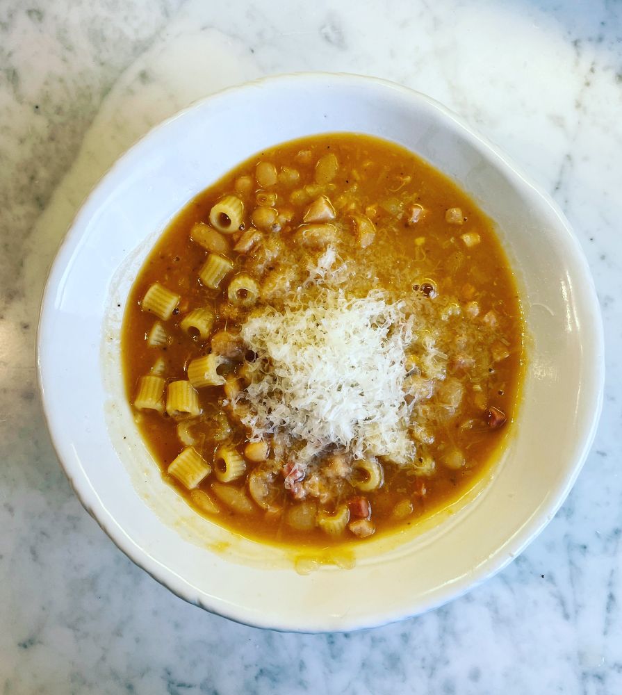 Nigella Lawson's absolutely perfect pasta fagioli soup in a white bowl on a white marble counter, with an obscene amount of grated parmesan on top