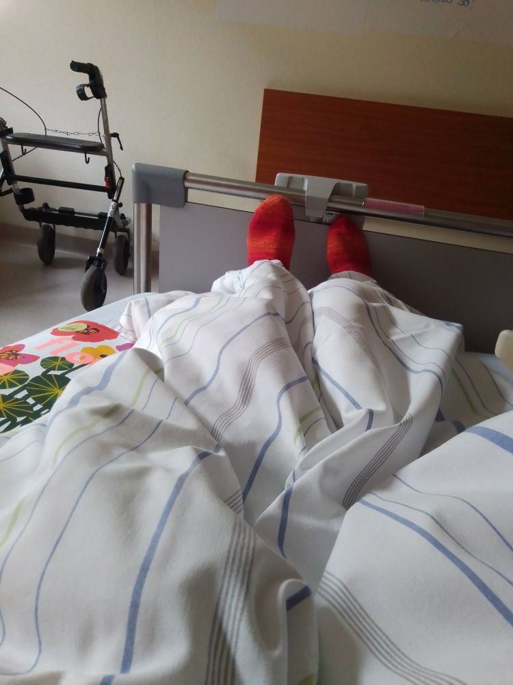 Krankenhausbett. Rote Socken gucken unter einer Decke raus.