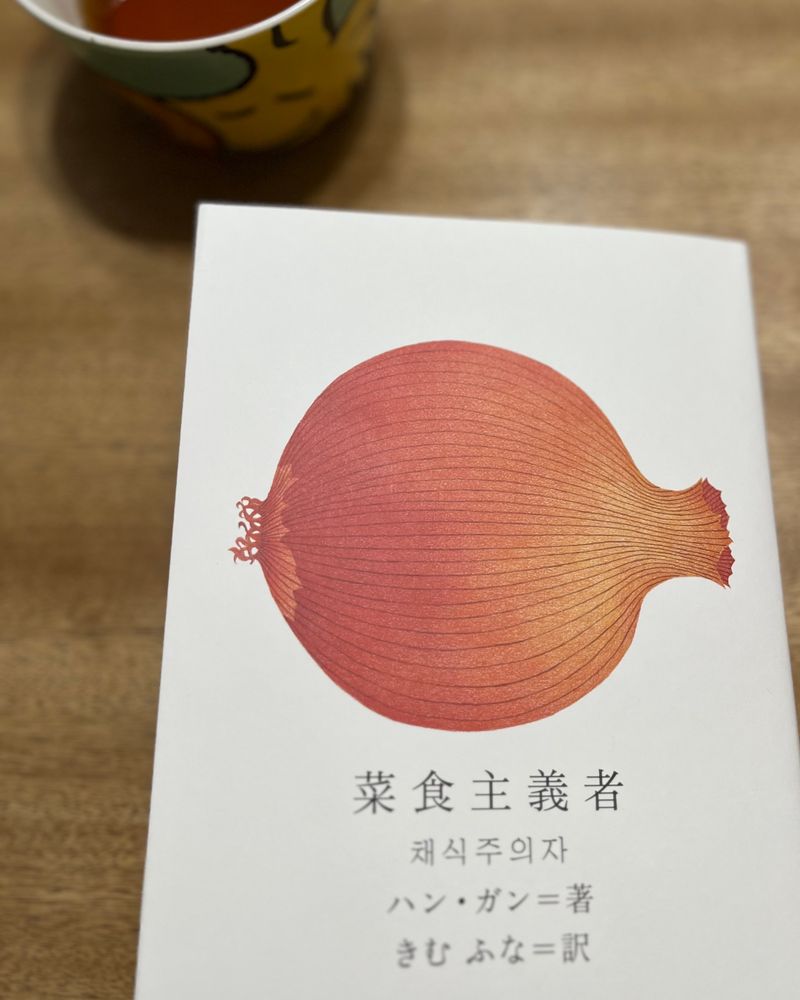 ハンガンの小説、菜食主義者の表紙の写真です。
テーブルの上にのっていて、右上にウッドストックの絵の描いたティーカップが写っています。