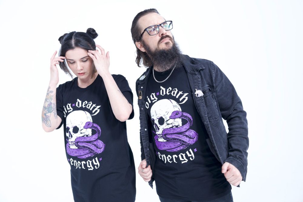 Two people, one masc, and one femme, dressed in Pepper Raccoon Big Death Energy t-shirts