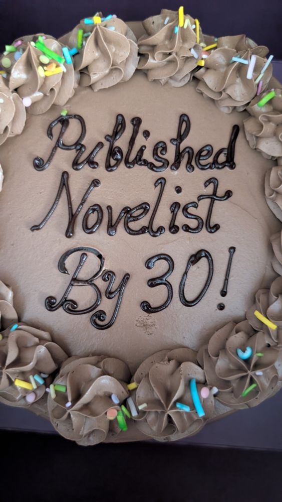A chocolate cake iced with the words "Published Novelist By 30!" 