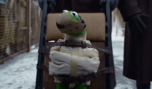 Kermit the Frog is strapped into a straightjacket and secured to a wooden board with leather straps, being wheeled outside in a snowy setting.