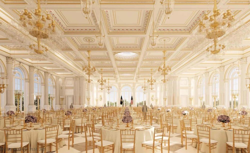 A lavish banquet hall with ornate gold-trimmed ceilings, grand chandeliers, and elegantly set round tables covered in cream linens and purple floral centerpieces. The space is filled with hundreds of identical golden chairs, but only a few human figures are present—and they appear oddly lifeless or artificial. Near the center aisle, two figures stand stiffly by the American flags, facing away from the viewer. Another figure is scattered near the sides, motionless, with an uncanny, mannequin-like presence. The people seem digitally inserted or rendered, contributing an eerie, surreal quality to an otherwise regal setting.
