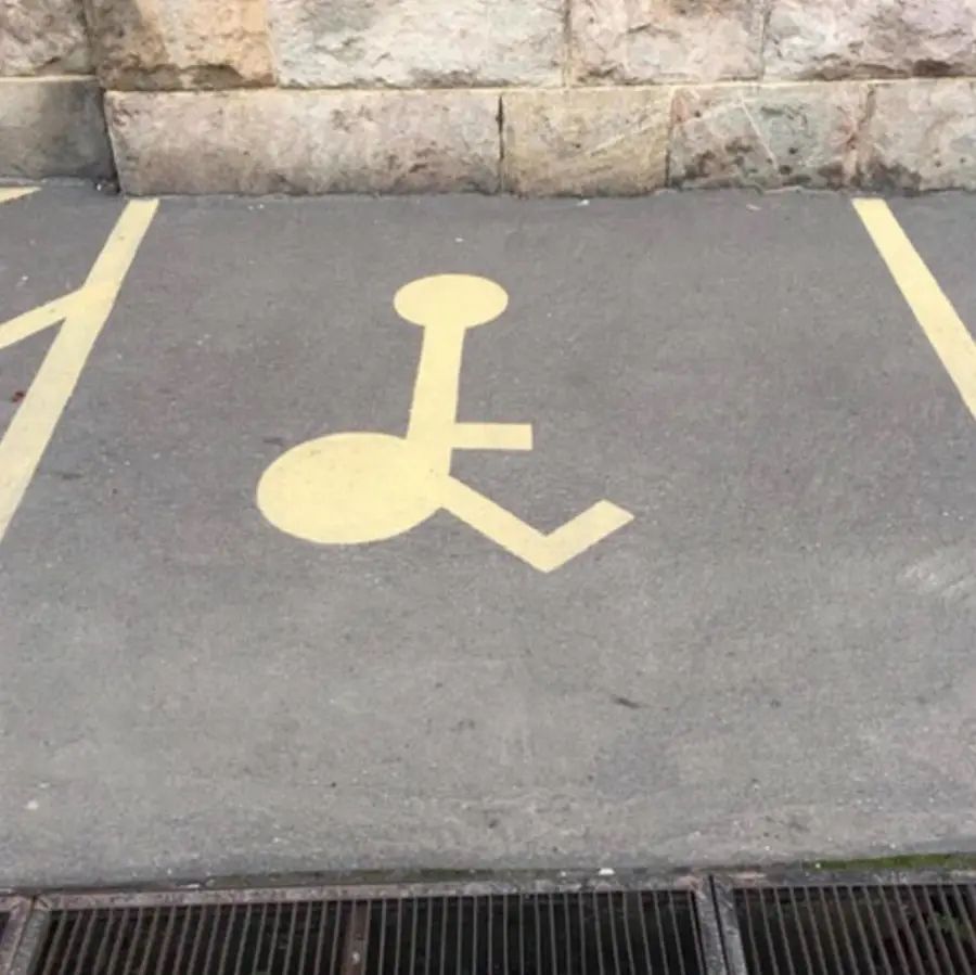 A misdrawn accessible parking symbol painted on the ground shows a stick figure with an oversized circular body and a small circle head, making the figure look awkwardly disproportionate.