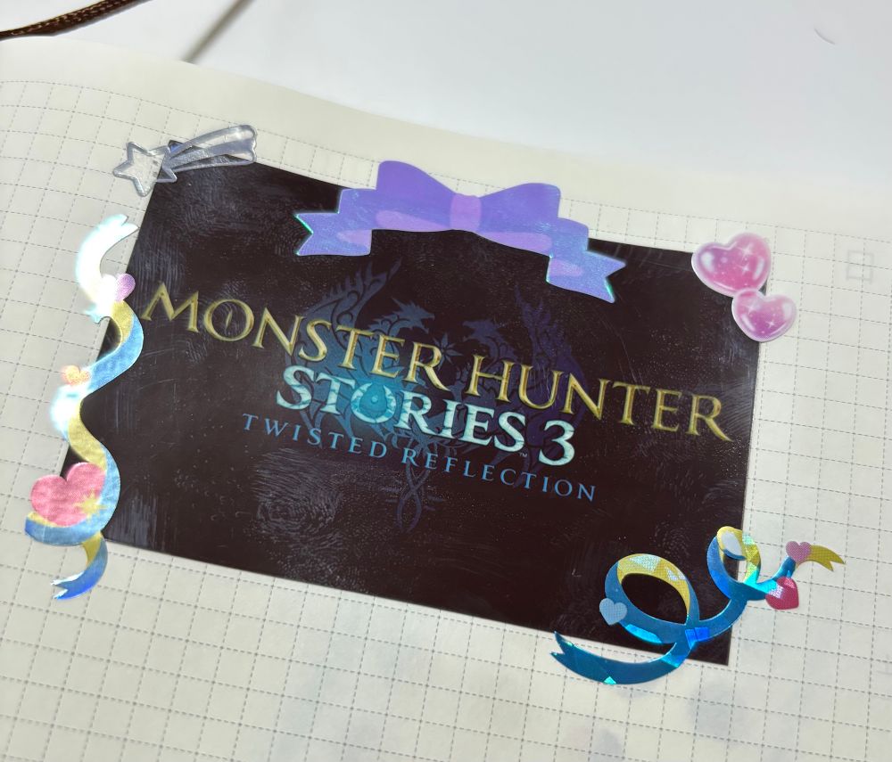 Photo of the monster hunter stories 3 logo printed onto a sticker and decorated with sparkly hearts and ribbons