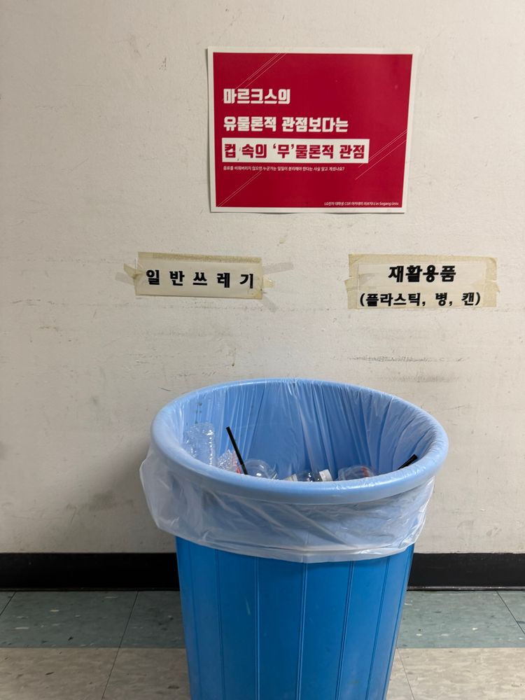 쓰레기통 위 벽에 포스터가 테이프로 붙어 있다. "LG전자 대학생 CSR 아카데미 리브지니"에서 부착한 포스터에는 "마르크스의 유물론적 관점보다는 컵 속의 무물론적 관점"이라는 메시지가 적혀 있다.