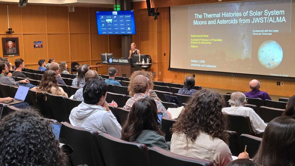 A speaker at a lectern presents "The Thermal Histories of Solar System Moons and Asteroids from JWST/ALMA" to an audience in a lecture hall. The presentation screen displays images of moons and graphs.