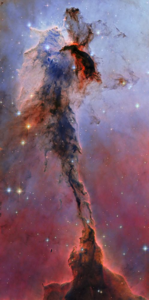 A very vertical image of a tall, thin portion of a nebula that appears to stand like a tree. The top is made up of large brown and blue pale clouds and dust that look like voluminous hair. To the right of the clouds is a dark rugged shape, surrounded by a bright red light. Below the clouds is a dark stem, made of tendrils of dust, wrapping around themselves to the bottom of the image, where the tendrils widen and expand like a tornado-like dust cloud. The background has several stars of different colors and sizes, and the shade of the background changes from light blue at top to dark red at the bottom.