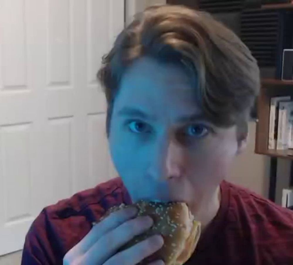 a man is eating a hamburger with sesame seeds on it while looking at the camera .