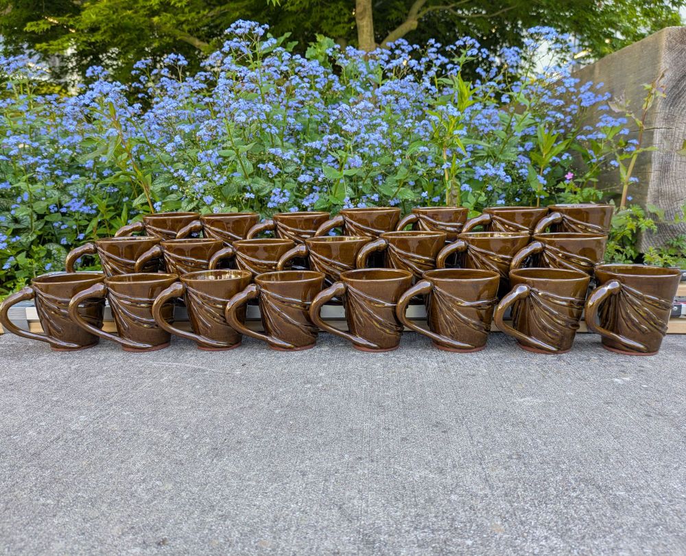 A three tiered display of brown mugs featuring handles that look like bull kelp stipes and blades that wrap around the mug body 
