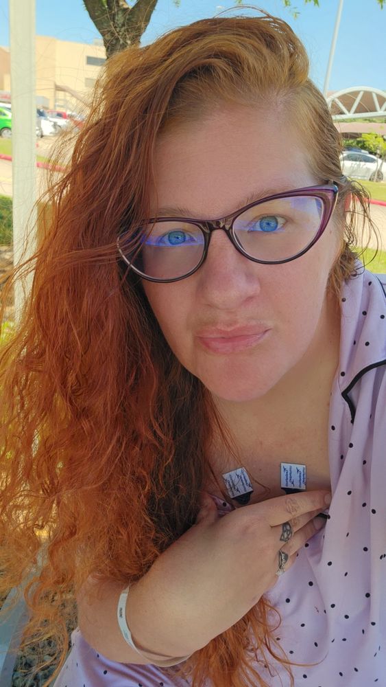 Red headed woman in pink pajamas showing two EKG lead stickers on her chest 