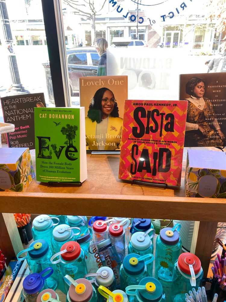 A winds display of books showcasing books by or about women- Eve, Lucky One, Heartbreak is the National Anthem, Sista Said, and A Passionate Mind in Relentless Pursuit 