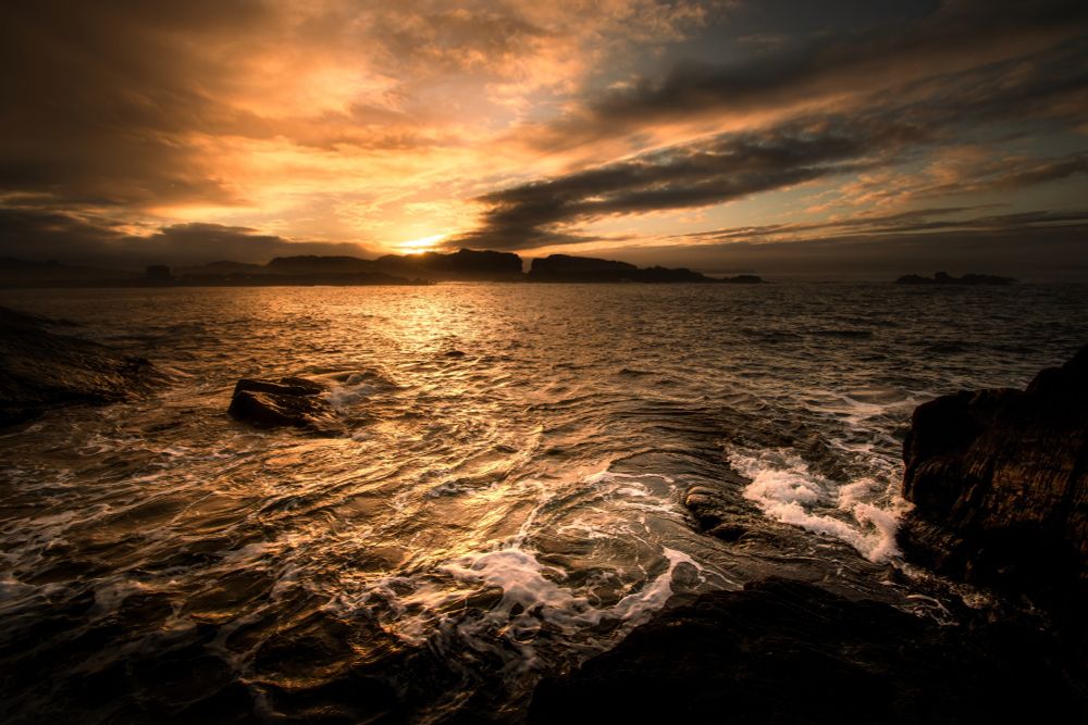 A depiction of a sunset over water with dramatic coastlines in the background