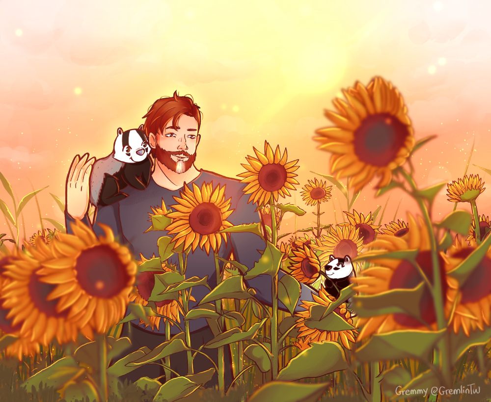 Badjhur in a field of sunflowers, smiling, with a sunset in the background. Brock is on his right shoulder, Biscuit in his left hand. 