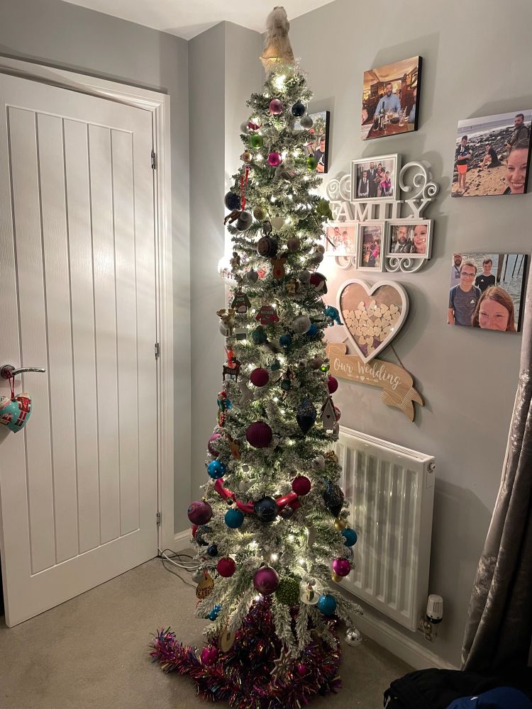 A well decorated and lit artificial Christmas tree with tinsel at the base