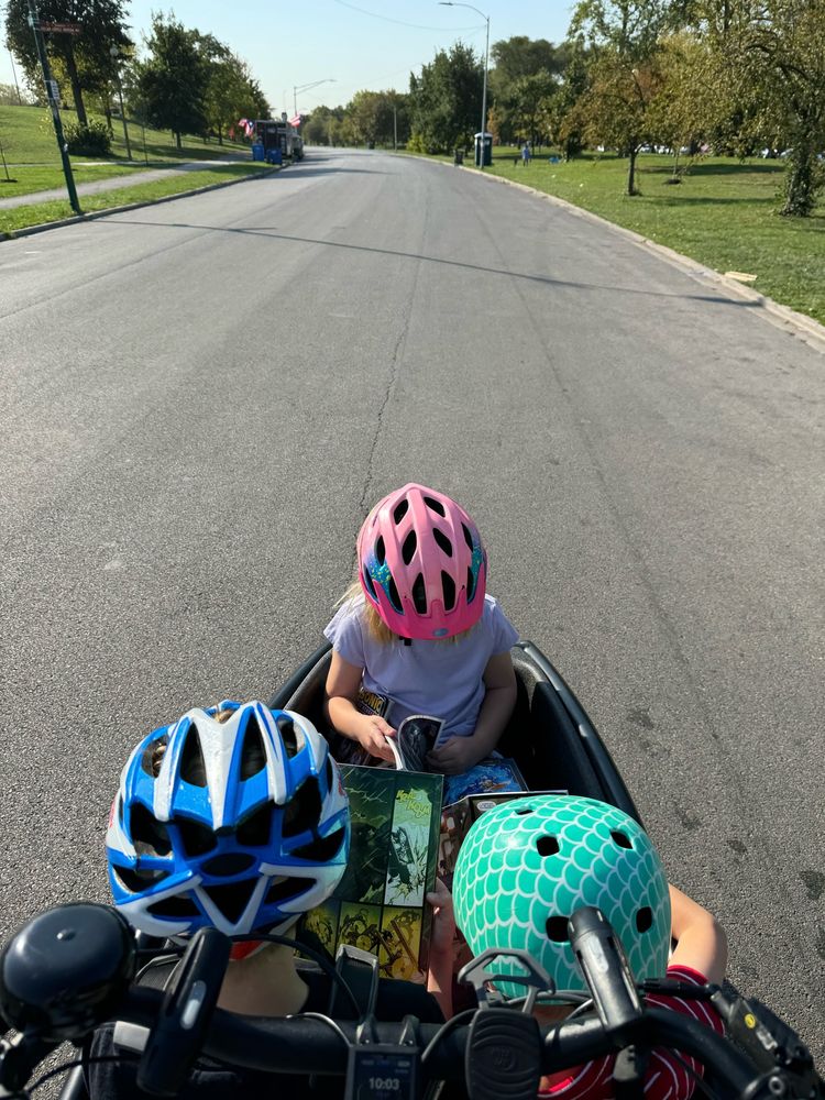 Kids reading library books in a cargo bike, rolling through one of Chicago’s awesome parks