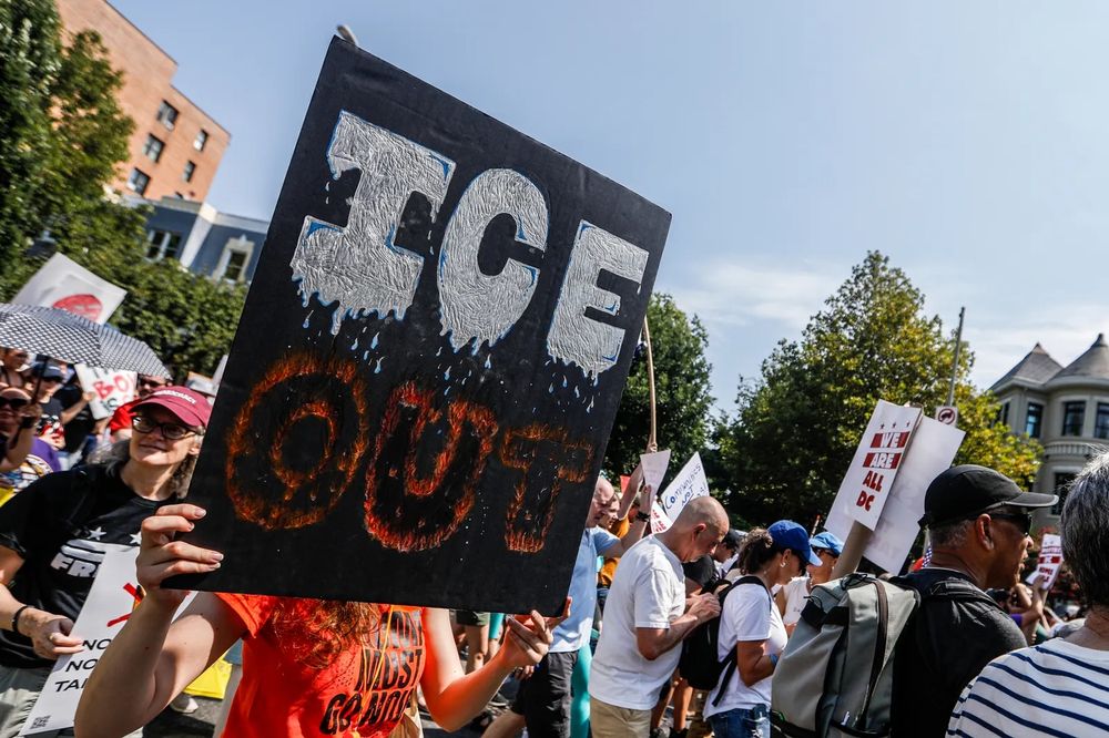 A protestor in a crowd holds a a black sign that says 