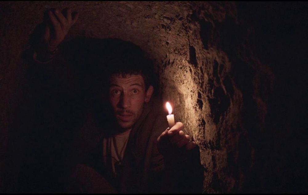 A man in a cave holding a candle in the film la chimera
