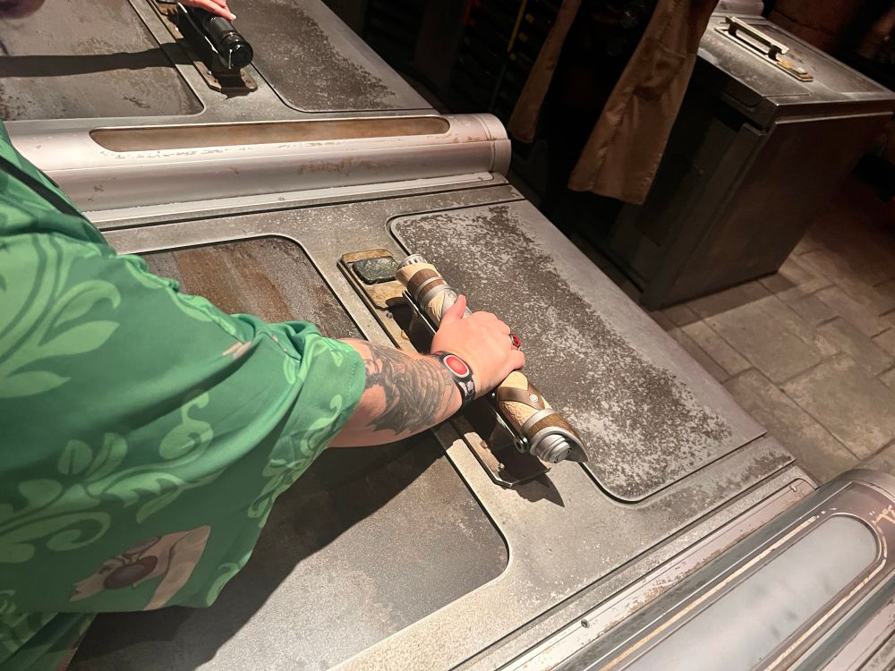 Builder’s hand resting on a saber hilt that sits on a stand on the build table