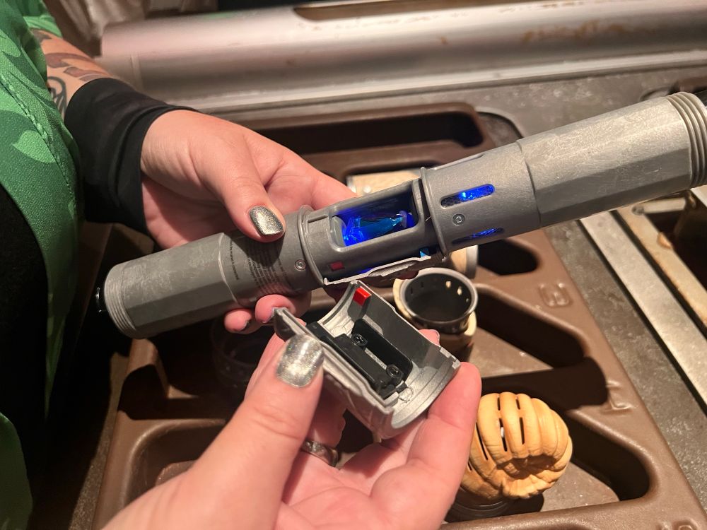 Closeup of hands holding a lightsaber base and adding parts to it.