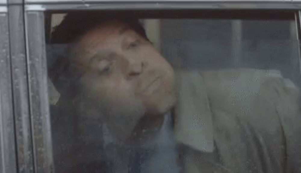 a man in a suit and tie is looking out of a car window .