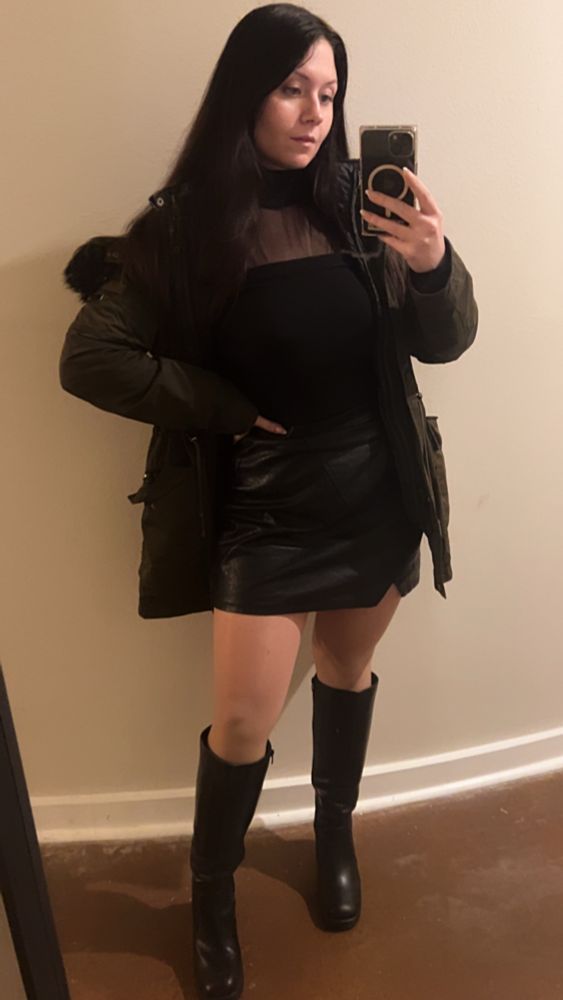 Jamie wearing a dark green parka with black fur hood, mesh black bodysuit, black leather miniskirt with a slight notch above her right knee, and knee-high black gogo boots
