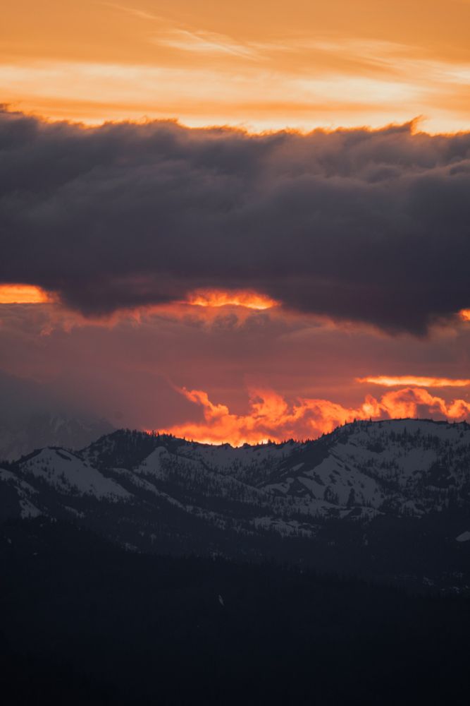 An orange sunset over the mountains with clouds behind the mountains that look like fire.