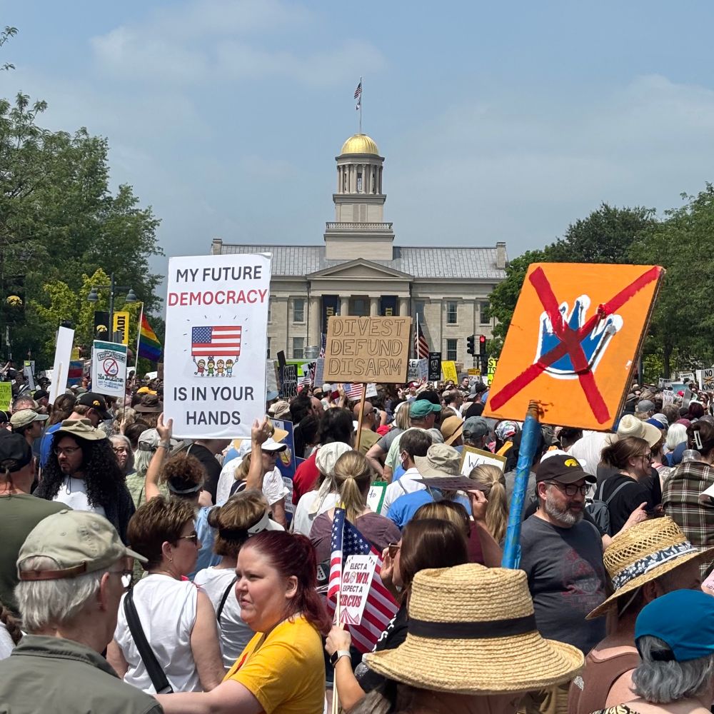 Iowa Avenue in Iowa City crowded with protesters carrying signs with various anti-Trump messages. The Old Capitol stands in the background. 