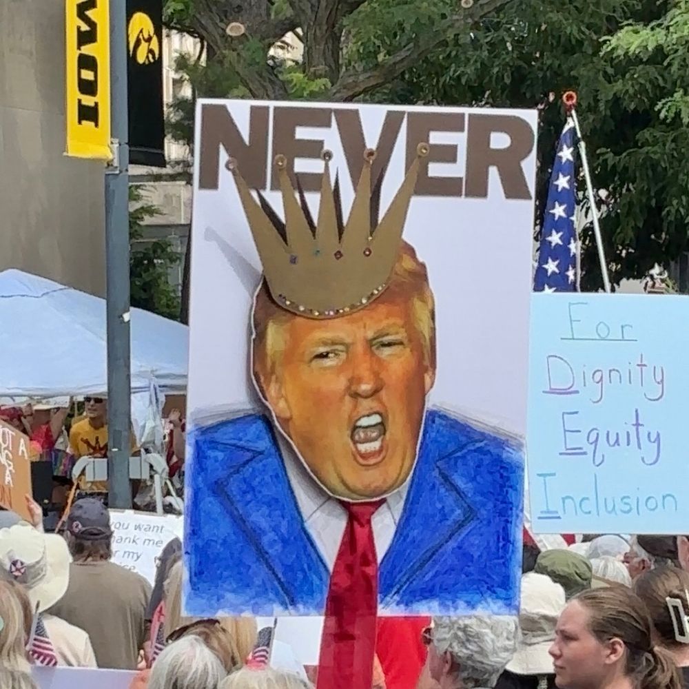 A sign depicting Donald Trump in his usual blue suit and red tie adorned with a crown. The word NEVER appears above his image. 