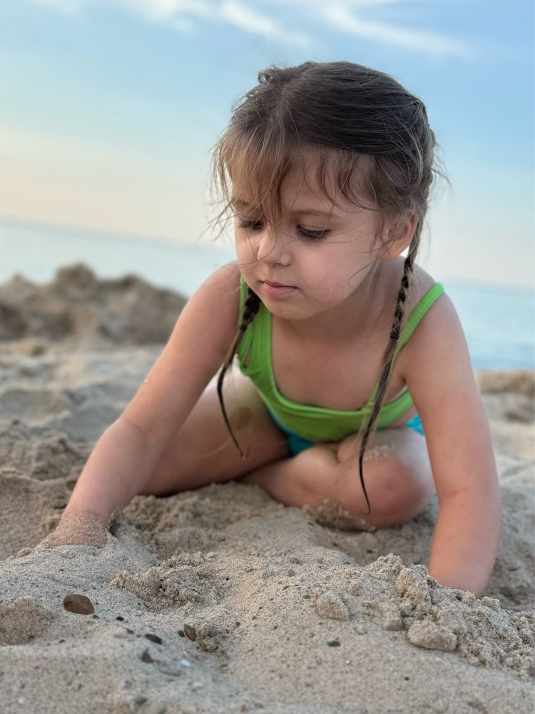 A young girl digging her hands in the sand at the beach 