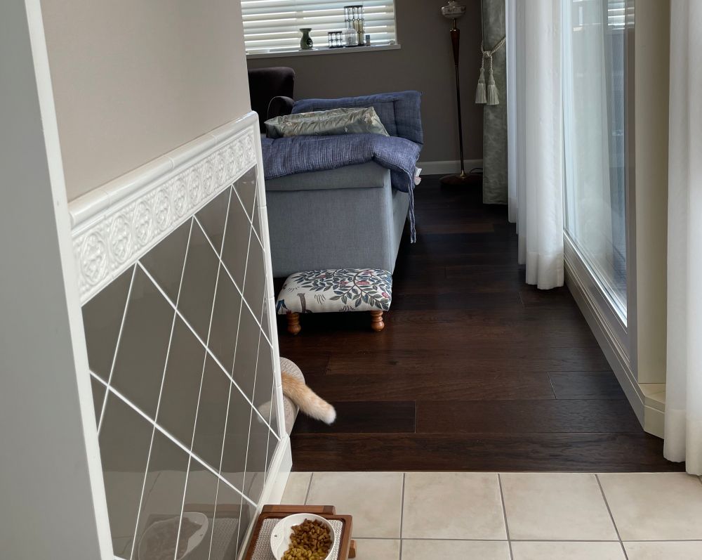 ダイニングルームからリビングルームを臨む写真。壁の向こう側の爪とぎのうえに寝ている猫の尻尾だけが見えている。
