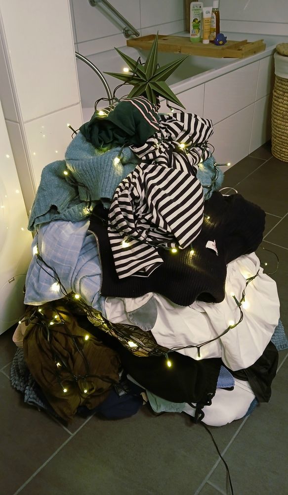 Ein Foto aus einem Badezimmer. Dort liegt ein aufgetürmter Dreckwäscheberg. Er ist geschmückt mit einer Lichterkette, an der Spitze steht ein grüner Stern. 