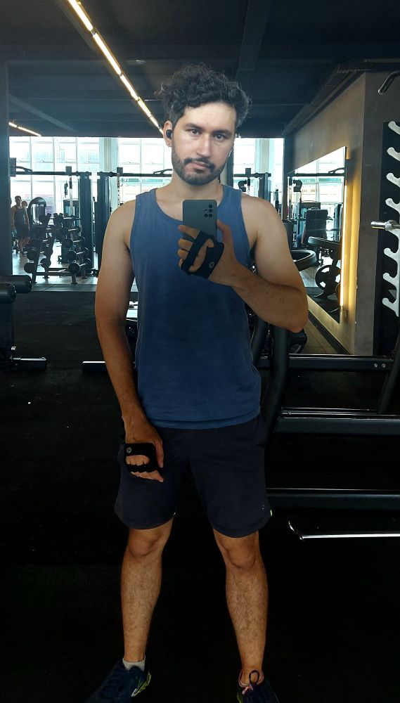 Homem segurando celular tirando selfie em frente a um espelho grande na academia