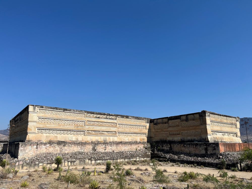 Vista frontal de las ruinas de Mitla. Un edificio de piedra alargada con grabados en las paredes exteriores.