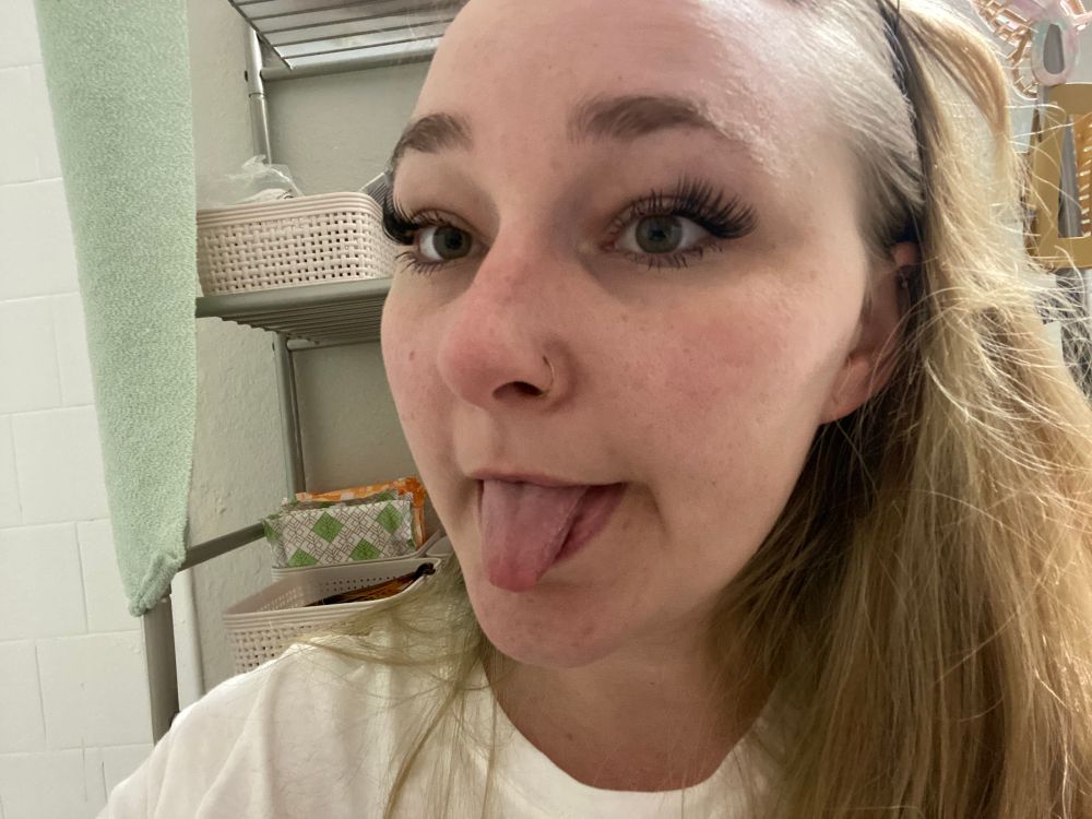 Flossy jane takes a selfie with her tongue out. She has Not expertly placed fake lashes on her eyes lol 