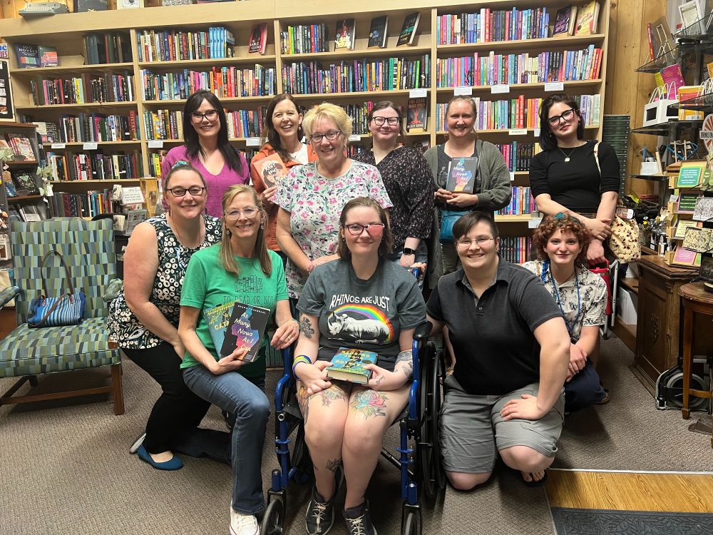 A photo of 11 readers including the author Shana Youngdah, several people are holding copies of the novel As Many Nows As I Can Get. There are bookshelves behind them. 