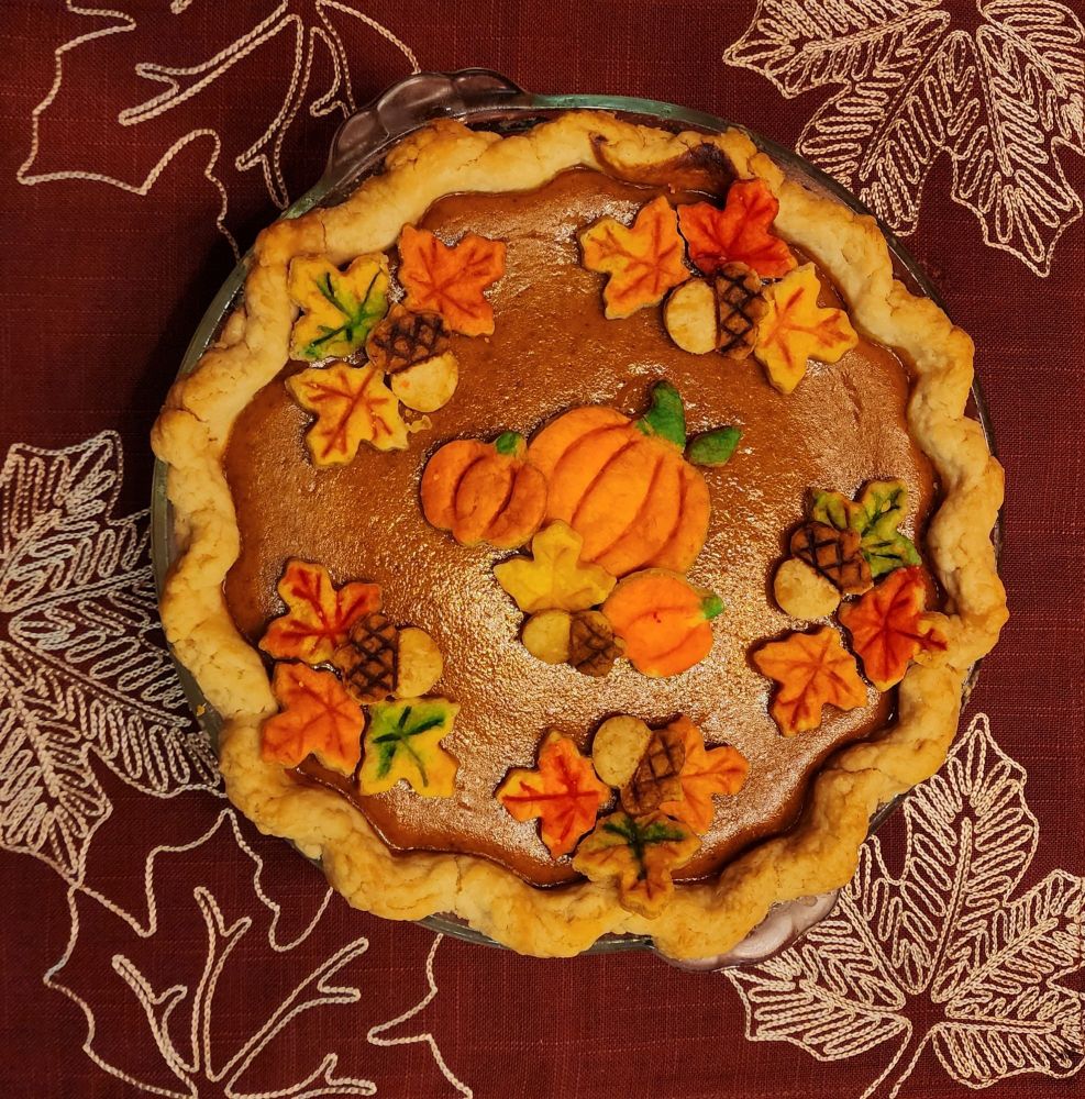 Pumpkin pie topped with fall-colored leaves, acorns, and pumpkins cutouts