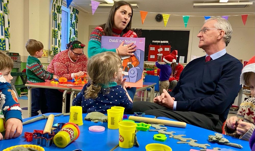 Hilary Benn sitting at the play dough table with children from Naíscoil na Seolta, talking to the Naíscoil leader.  