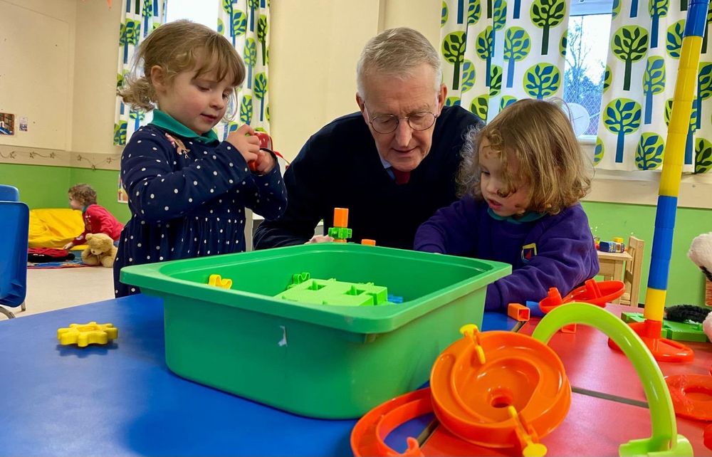 Hilary Benn sitting with children from Naíscoil na Seolta with toys. 